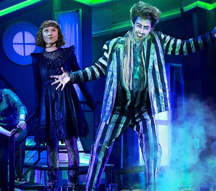 Beetlejuice: Theatrical scene with four performers in colorful lighting, featuring a person in a striped suit and exaggerated makeup.